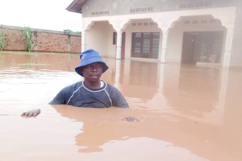 Ein Mann steht bis zur Brust im braunen Wasser vor einem überschwemmten Gebäude