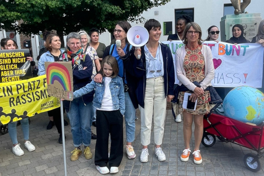 Es ist eine Gruppe von Demonstrierenden zu sehen, die Banderolen mit Aufschriften wie „Kein Platz für Rassismus” tragen.