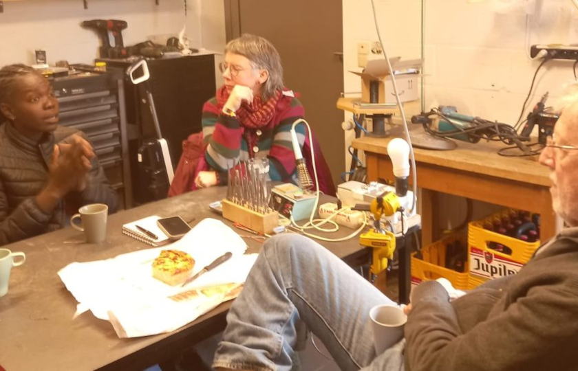 3 Personen im Gespräch, um einen Tisch in einer Werkstatt